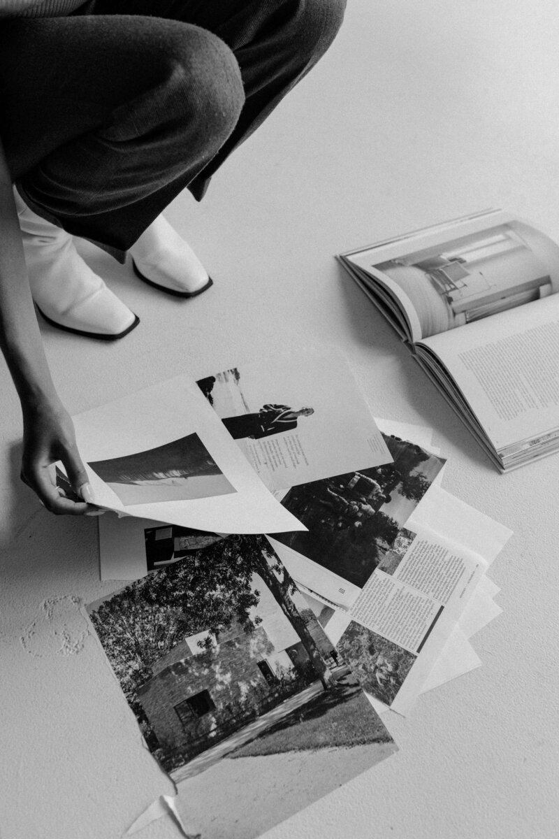 Black and white photo of a woman's hands arranging pages and photographs on the floor