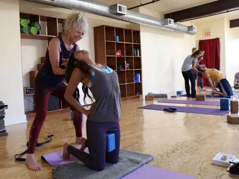 Students learning therapeutic camel pose assists during yoga therapy training California