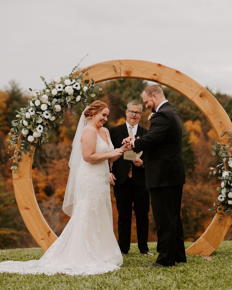 bride reading vows to her groom in the fall, round wooden arch with white roses
