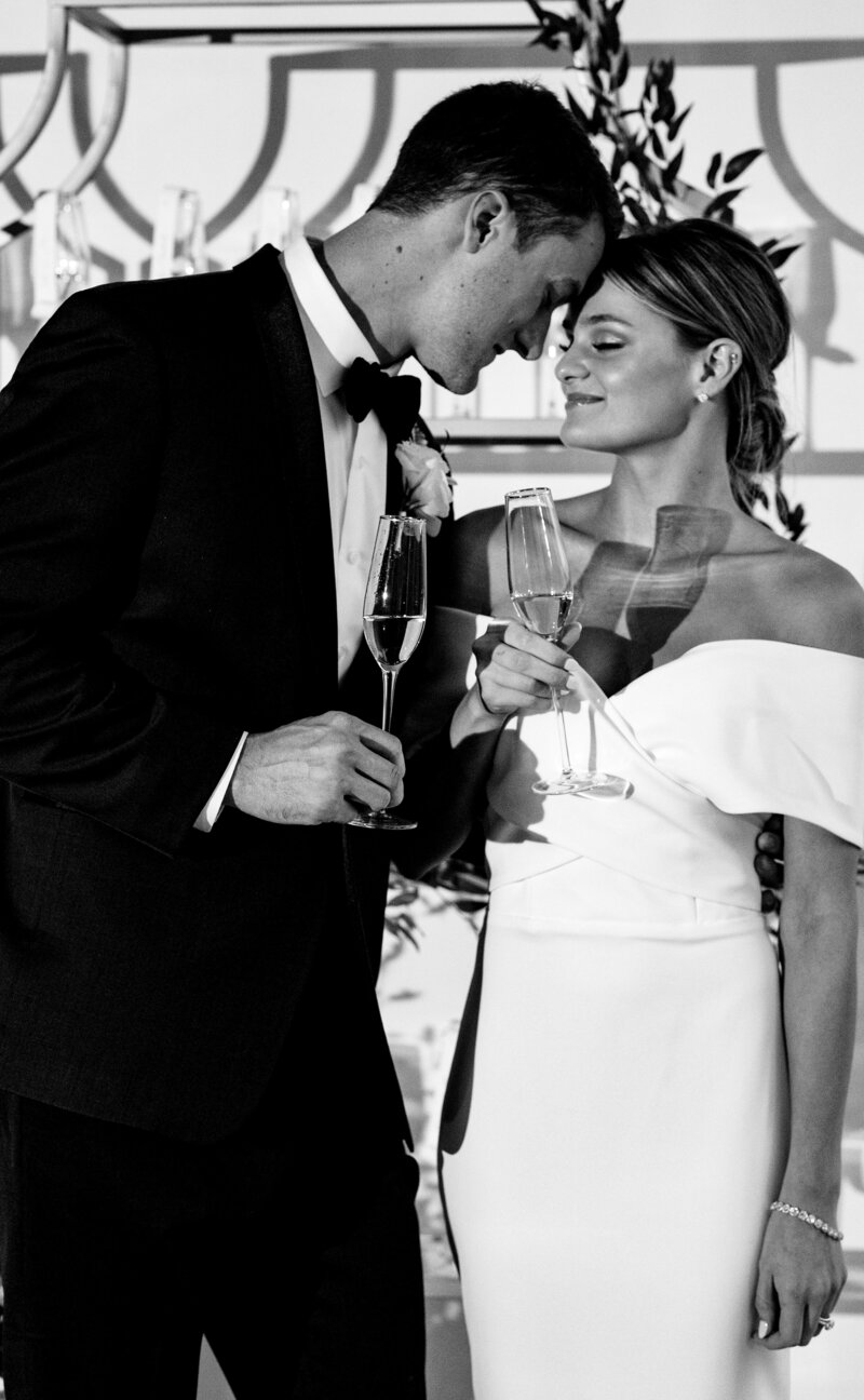 black and white picture of an extremely elegant caucasian couple in their black tie wedding enjoying a glass of champagne.