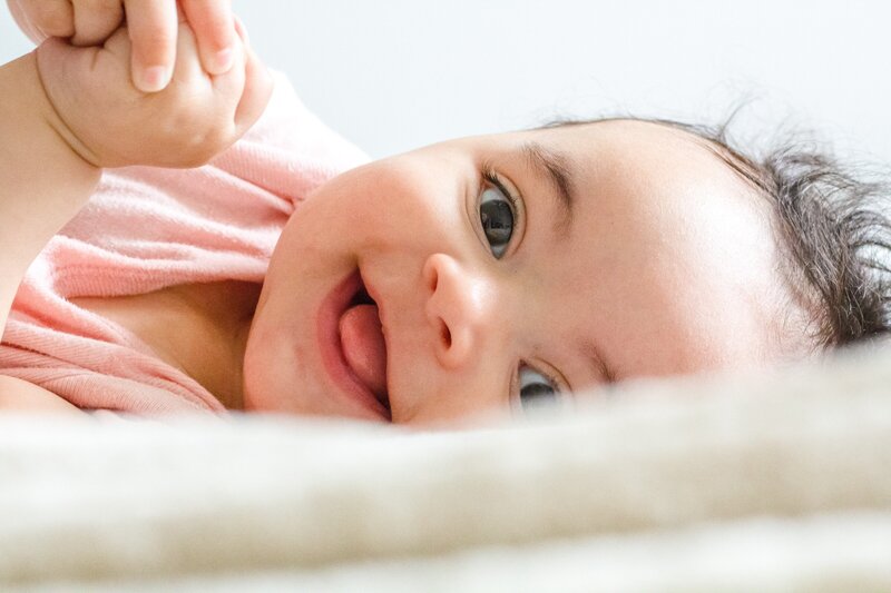baby sitting up looking away while holding a toy