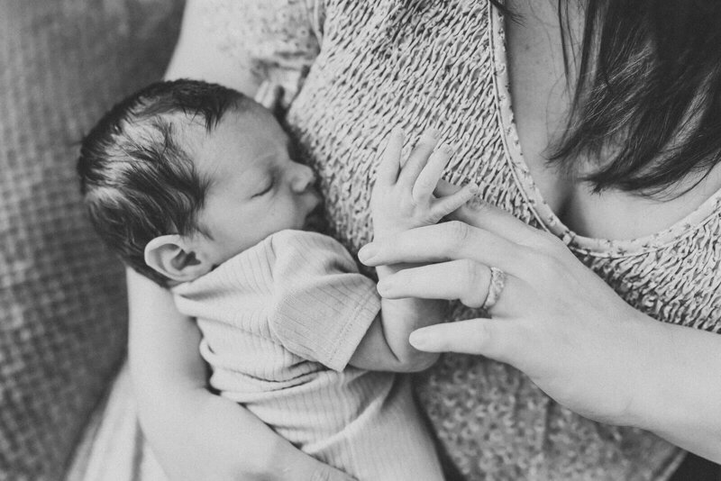 A serene newborn baby is sleeping, wrapped snugly in a soft, neutral-toned fabric. The baby has closed eyes and a calm expression, lying against a gentle, textured backdrop that enhances the cozy atmosphere.