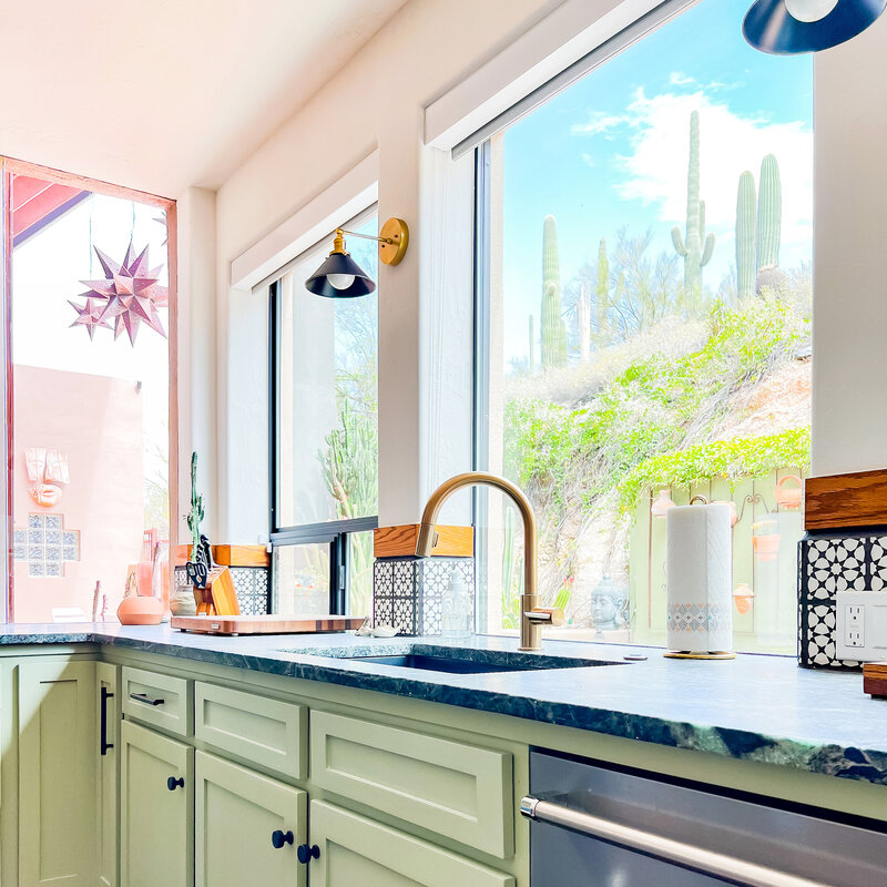 Sink in a colorful kitchen with sage green cabinets with beautiful views of many saguaro cacti.