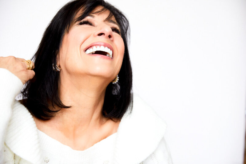 Isabella laughing with hand in hair wearing white sweater