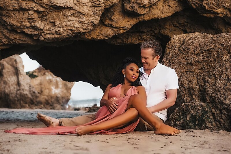 Couple sits against rocks on a beach
