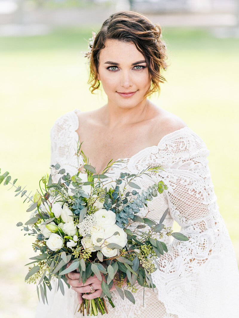 bride smiles at camera while holding green and white bouquet