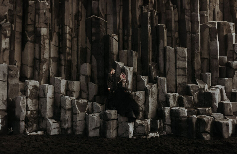 An elopement couple wearing all black standing on basalt pillars at Iceland's black beach