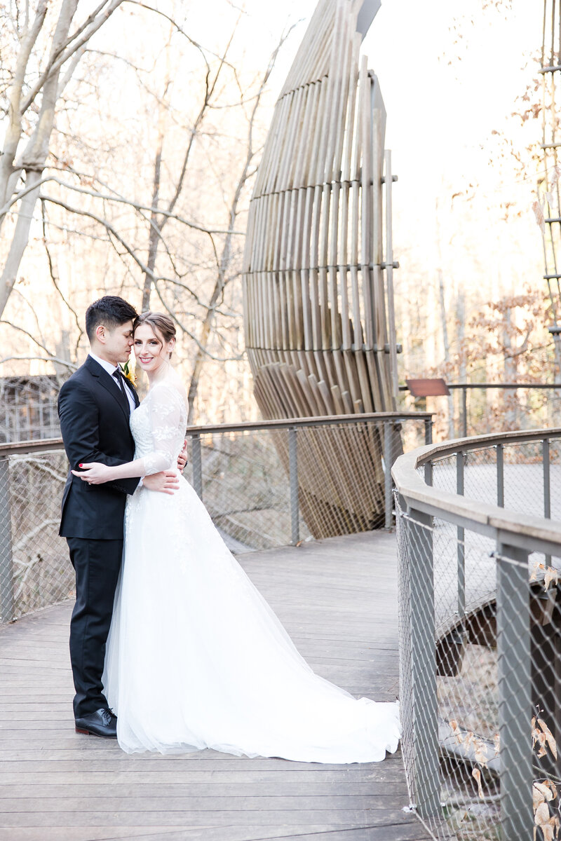 A bride and groom standing on a wooden bridge at Fernbank Museum Atlanta