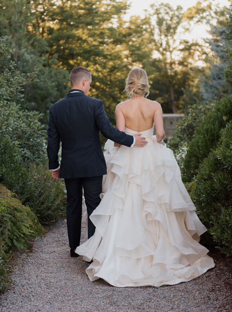 bride and groom walking through the gardens at crane estate on their summer wedding. bride is wearing a stunning ballgown.