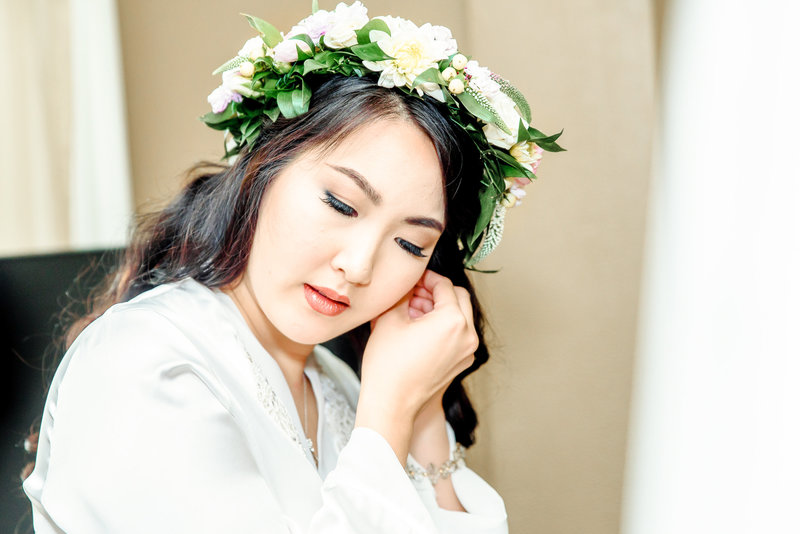 A bride wearing a floral head wreath puts in her earrings