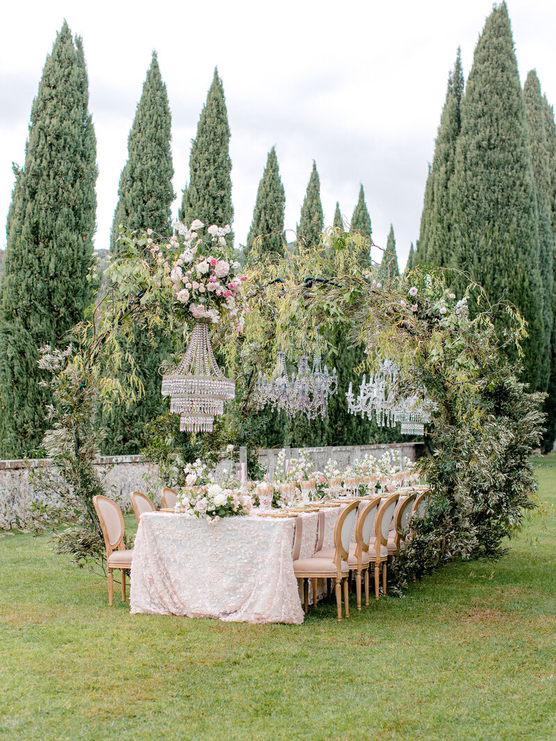 Al fresco pink table scape with crystal chandeliers with greenery and cypress trees in the background