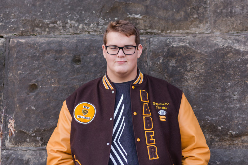 waynedale high school senior guy standing against a stone wall wearing his letterman jacket, photographed Downtown Wooster Ohio, photographed by Jamie Lynette Photography