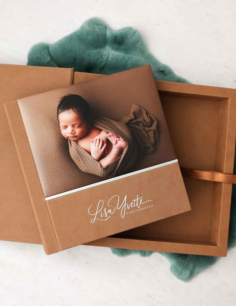 A beautifully designed custom photo album featuring a newborn wrapped in soft brown fabric on the cover. The album, branded with "Lisa Yvette Photography," is presented in a matching brown box, offering a stylish and timeless way to preserve precious memories.