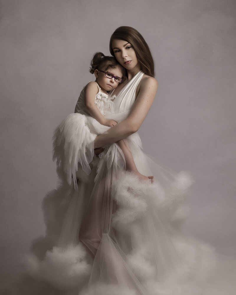 mother holding her daughter child wearing white tutu dress and fluffy gown standing on grey backdrop near seattle