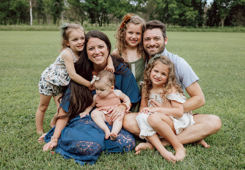 Family portrait of mom, dad, four sisters all sitting in the grass smiling at the camera taken by Jennifer Mosier Photography. 