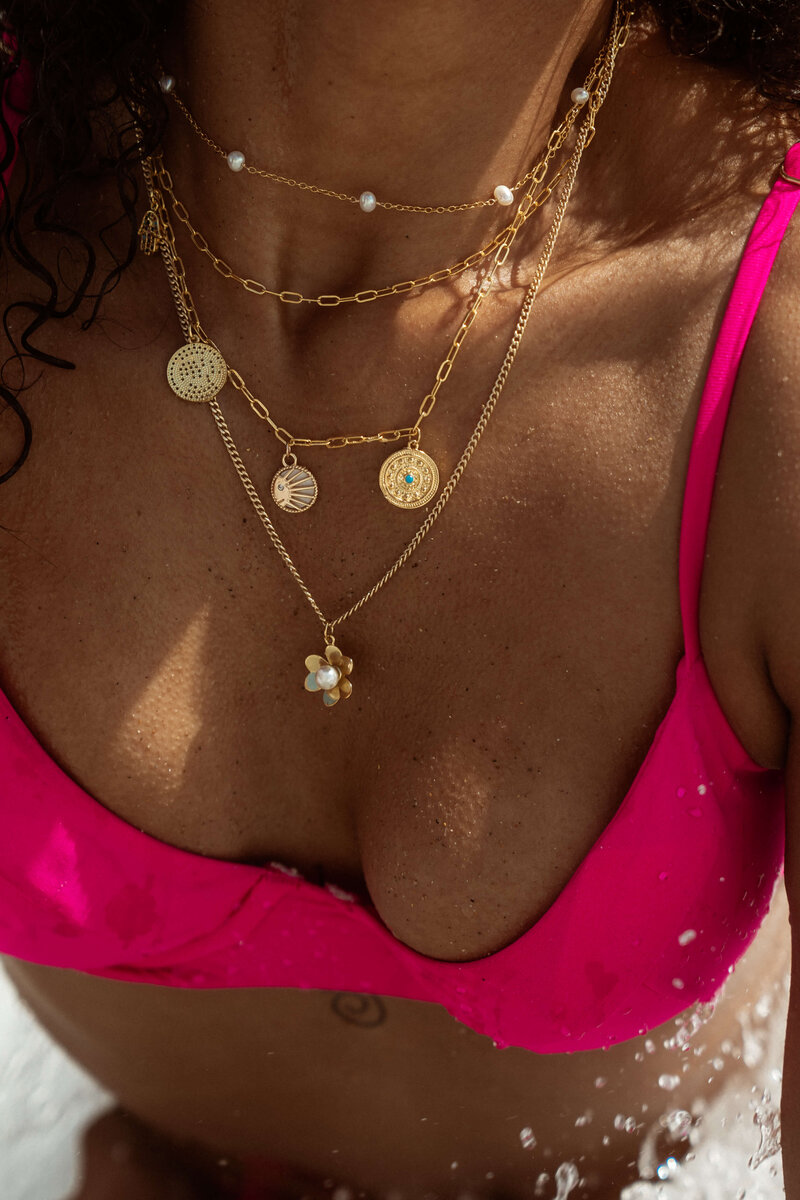 Stacked gold necklaces on model wearing pink swimsuit