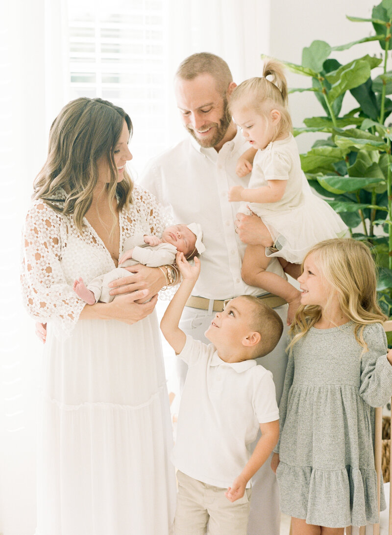 family of five snuggling their newborn baby sister during their Raleigh newborn portrait session. Photographed by Raleigh newborn photographers A.J. Dunlap Photography.