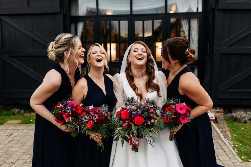 a bride and her bridesmaids laughing holding red bouquets