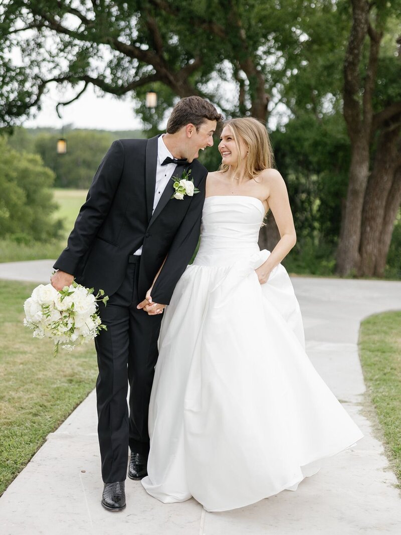 Bride and groom walking hand in hand down a garden path, smiling joyfully after their ceremony.