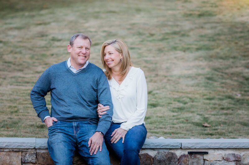 A couple sitting on a stone wall happy that they chose Salina Korn Photography for their family portraits.