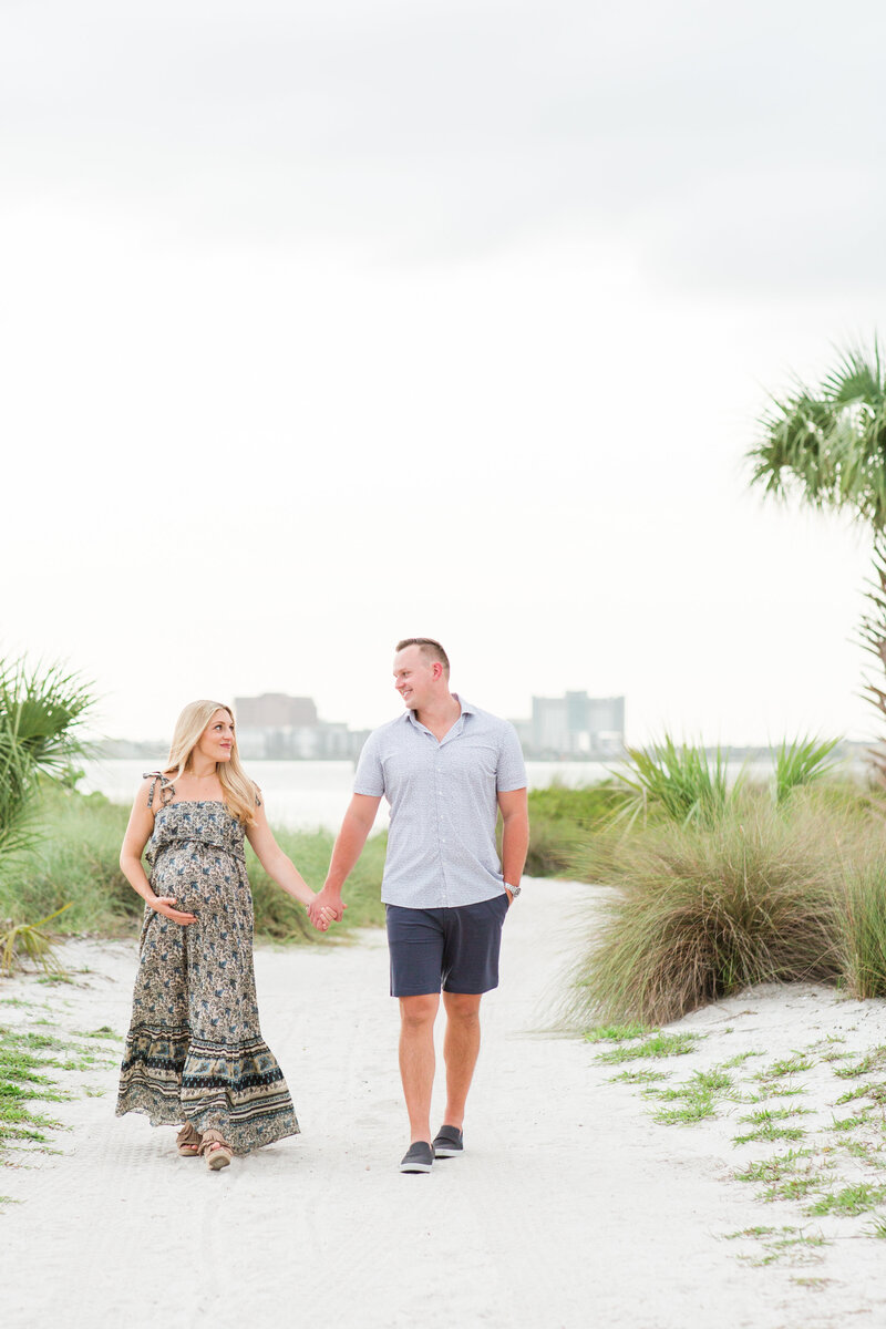 Pregnant mother holding hands with husband while walking on the beach in Tampa, Florida