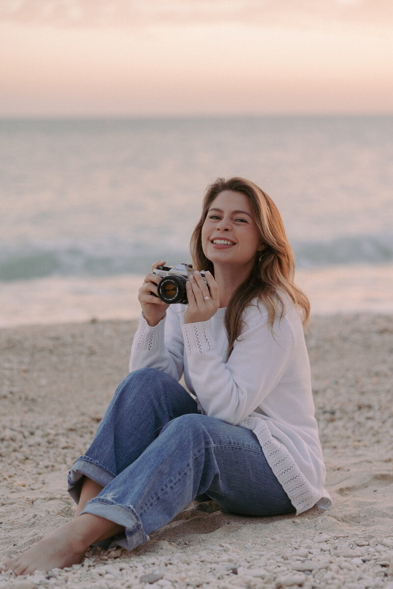 woman sitting on the beach smiling while holding a camera
