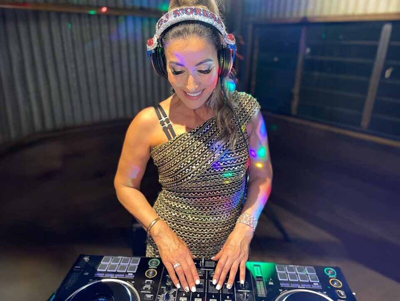 Female DJ wearing headphones and a one-shoulder patterned dress smiling while working the decks at an corporate event.