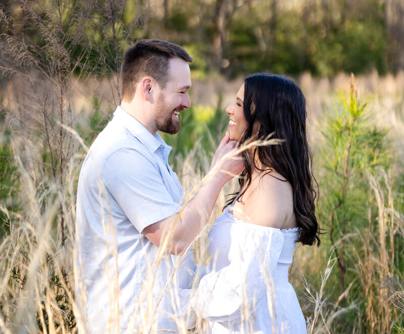 Newly engaged couple embracing and smiling at each other in a field of tall grass