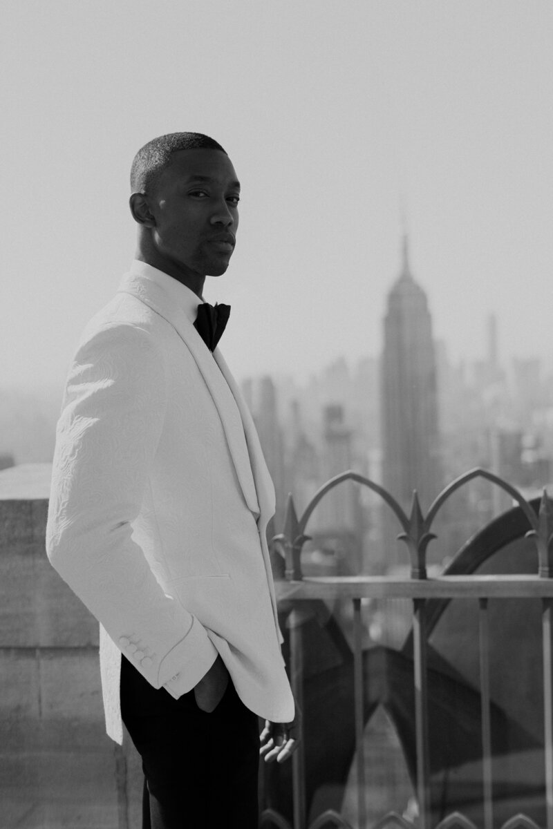 Groom in white tux jacket stands on the top of 30 Rock in NYC