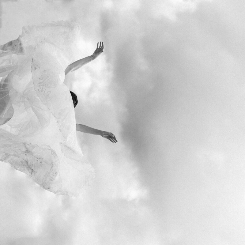 Black and white film photograph of bride throwing her wedding dress into the sky and floating down.