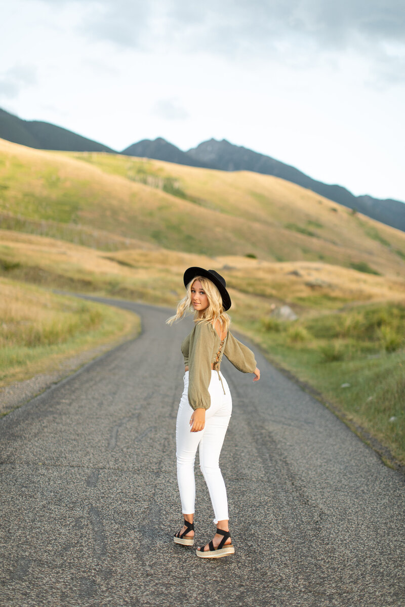 Walking on a mountainside road a young woman looks back.