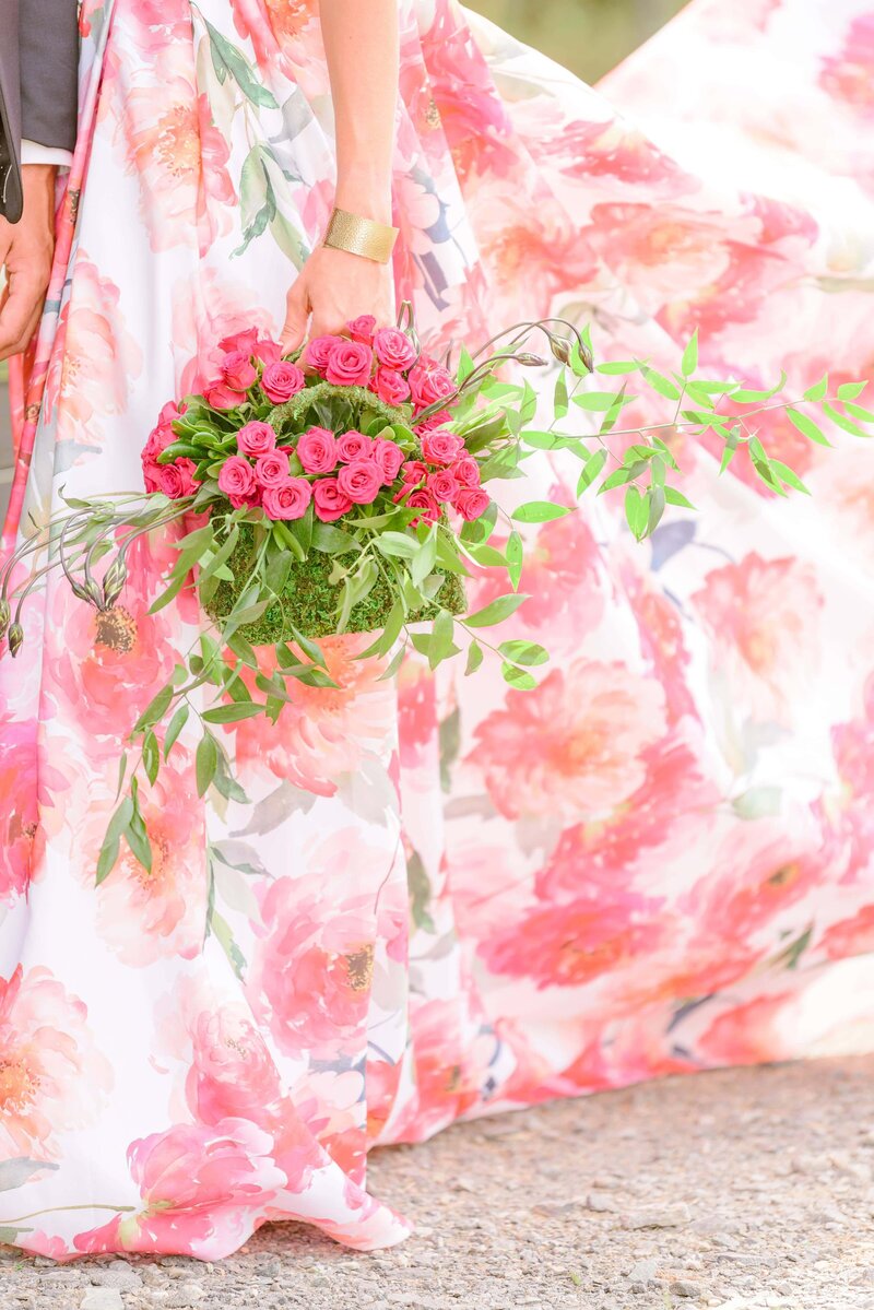 A purse overflowing with flowers is held in front of a pink floral dress.