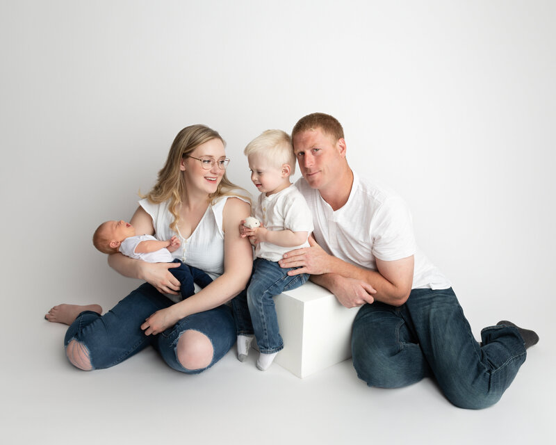 A clean and joyful family portrait featuring a toddler meeting their new sibling, styled in classic white tones for a timeless feel.