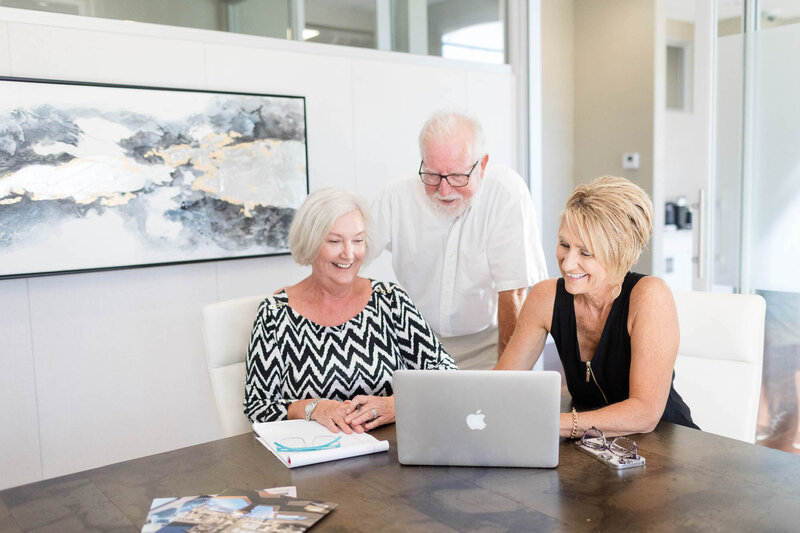 Woman on her laptop, smiling with two clients.