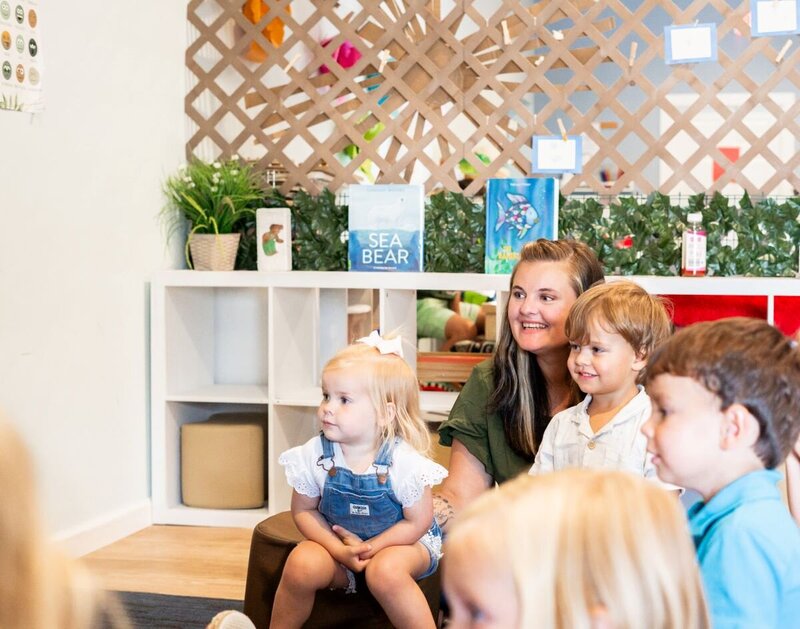 Ms. Heather sitting with toddler students on the floor of a classroom at the Nest, a preschool in Surf City, NC