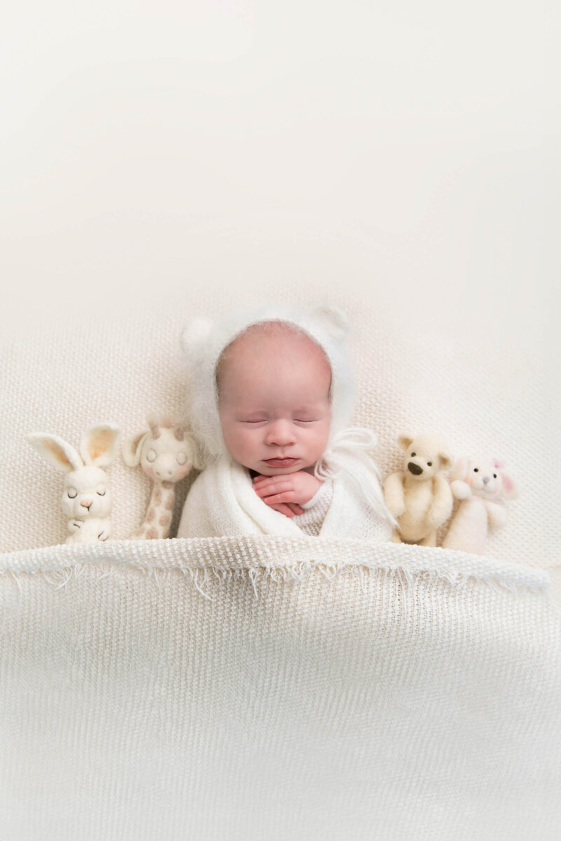 newborn baby girl wrapped in white with a white bear hat laying on a white background for her newborn photography session in Burlington, Ontario.