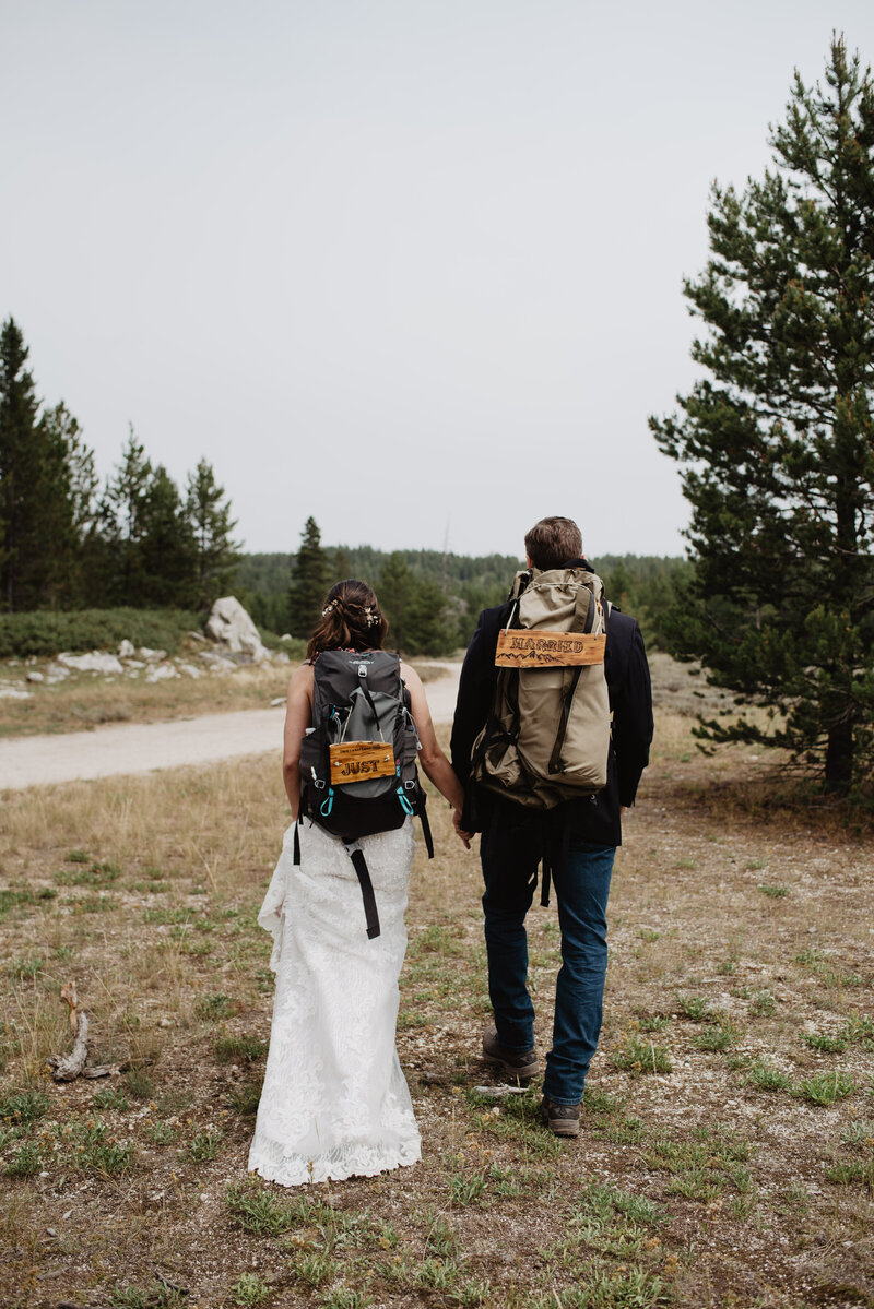 jackson hole photographers photographs bride adn groom with their hiking packs on their backs for their adventure wyoming elopement as they walk through the woods to a trail in the tetons