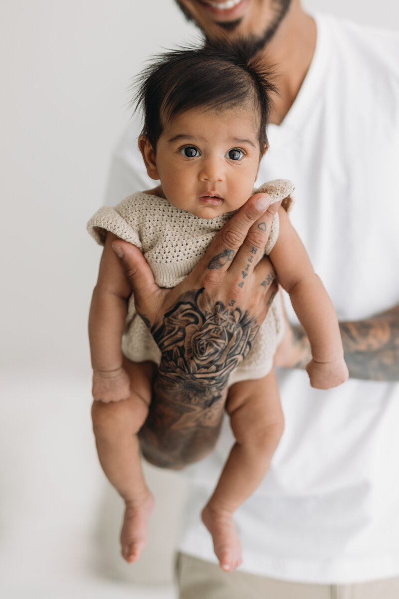 Newborn Portraits taken in Kelowna BC studio with dad holding baby in his hands and he has tatoos all over his hands and arms