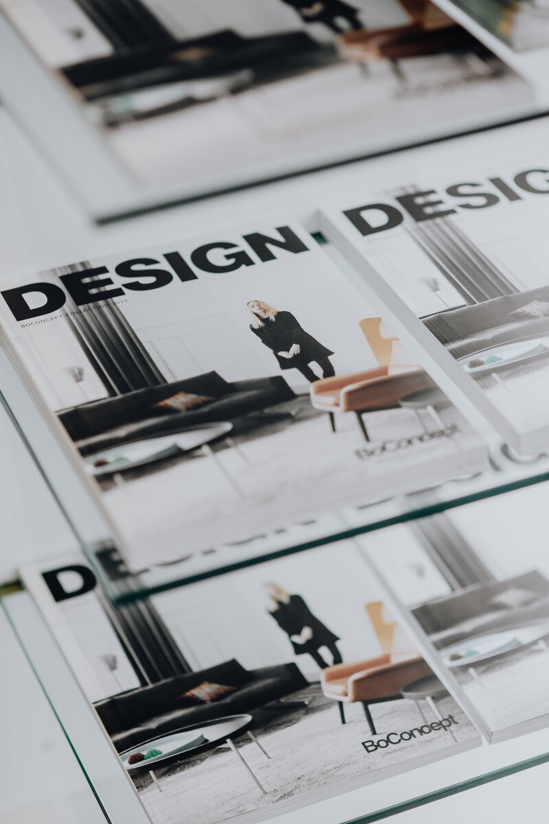 A close-up of a stack of neatly arranged design magazines placed on a white table. The magazines have stylish, minimalist covers, with soft shadows and a modern, clean aesthetic. The neutral tones and sleek design create a calm, organised workspace vibe.
