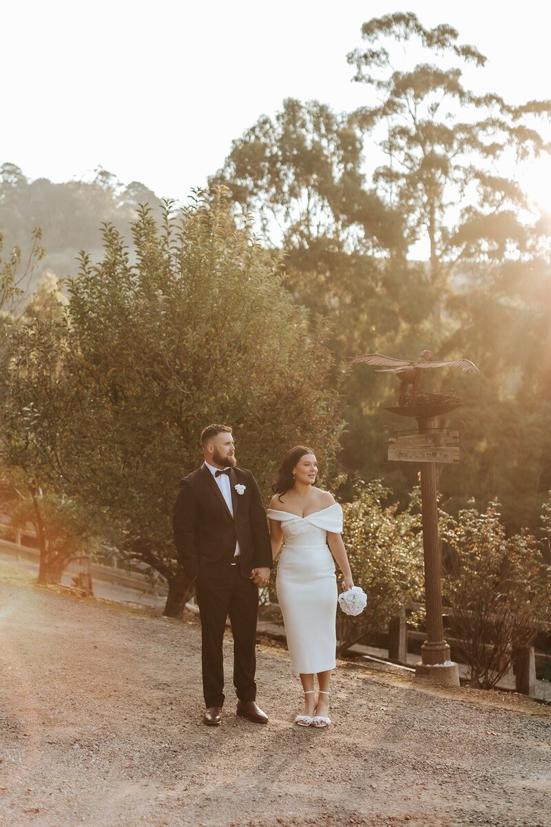 A bride and groom walking through autumn leaves