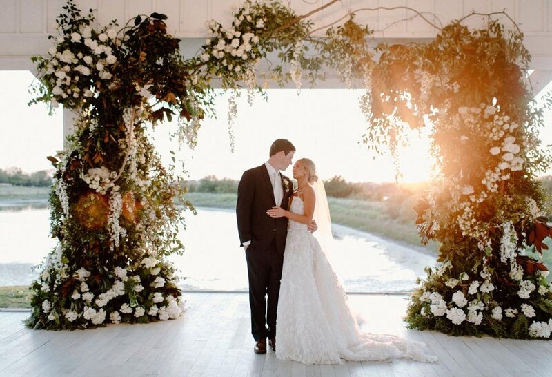 Bride and groom smiling at eachother under floral arch | CM Promotions wedding planning services in DFW