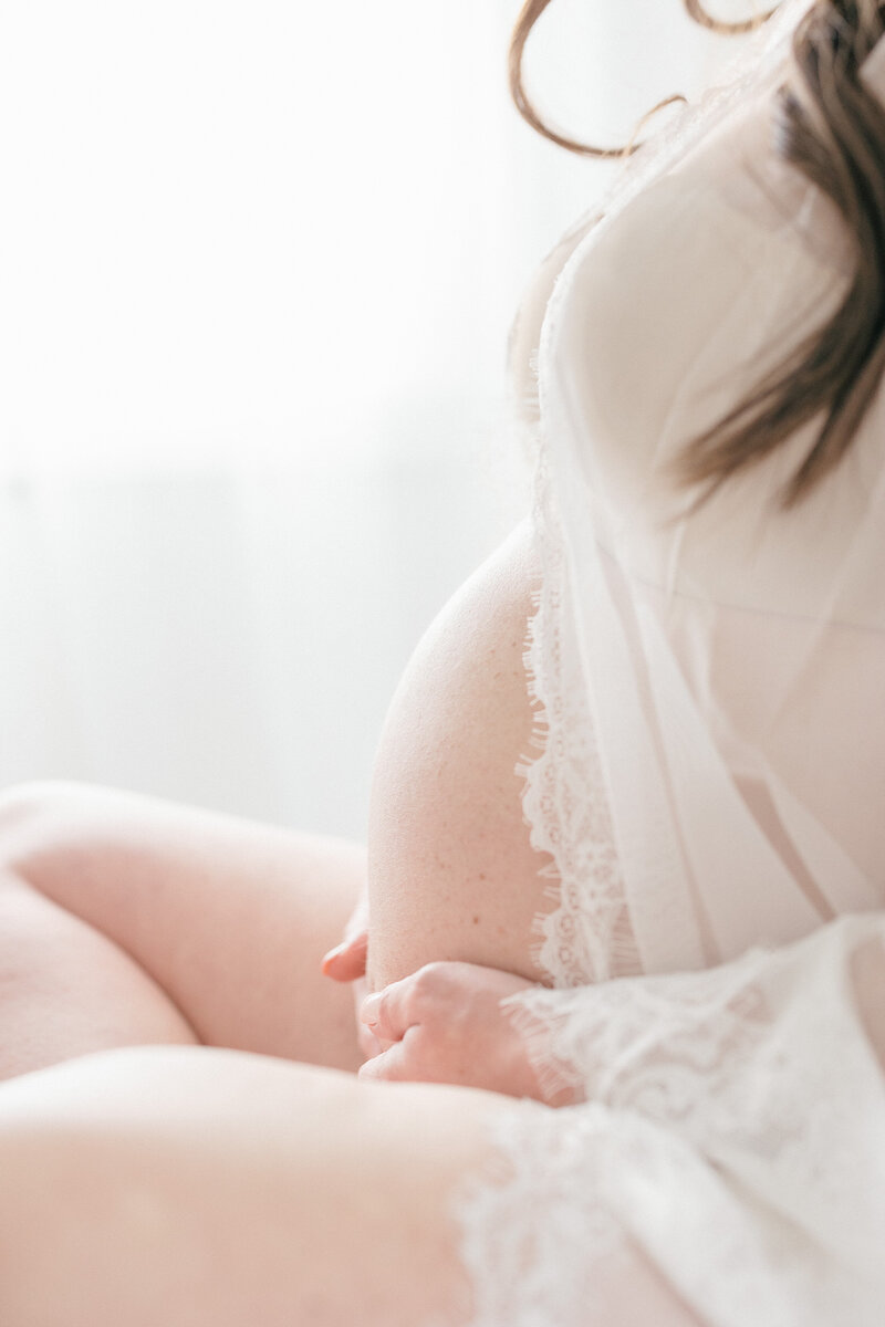 Pregnant woman cradling bare bump in all white studio in NJ