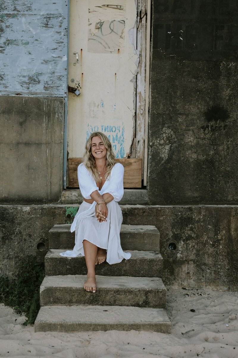 Women in white dress sitting on stairs by the beach