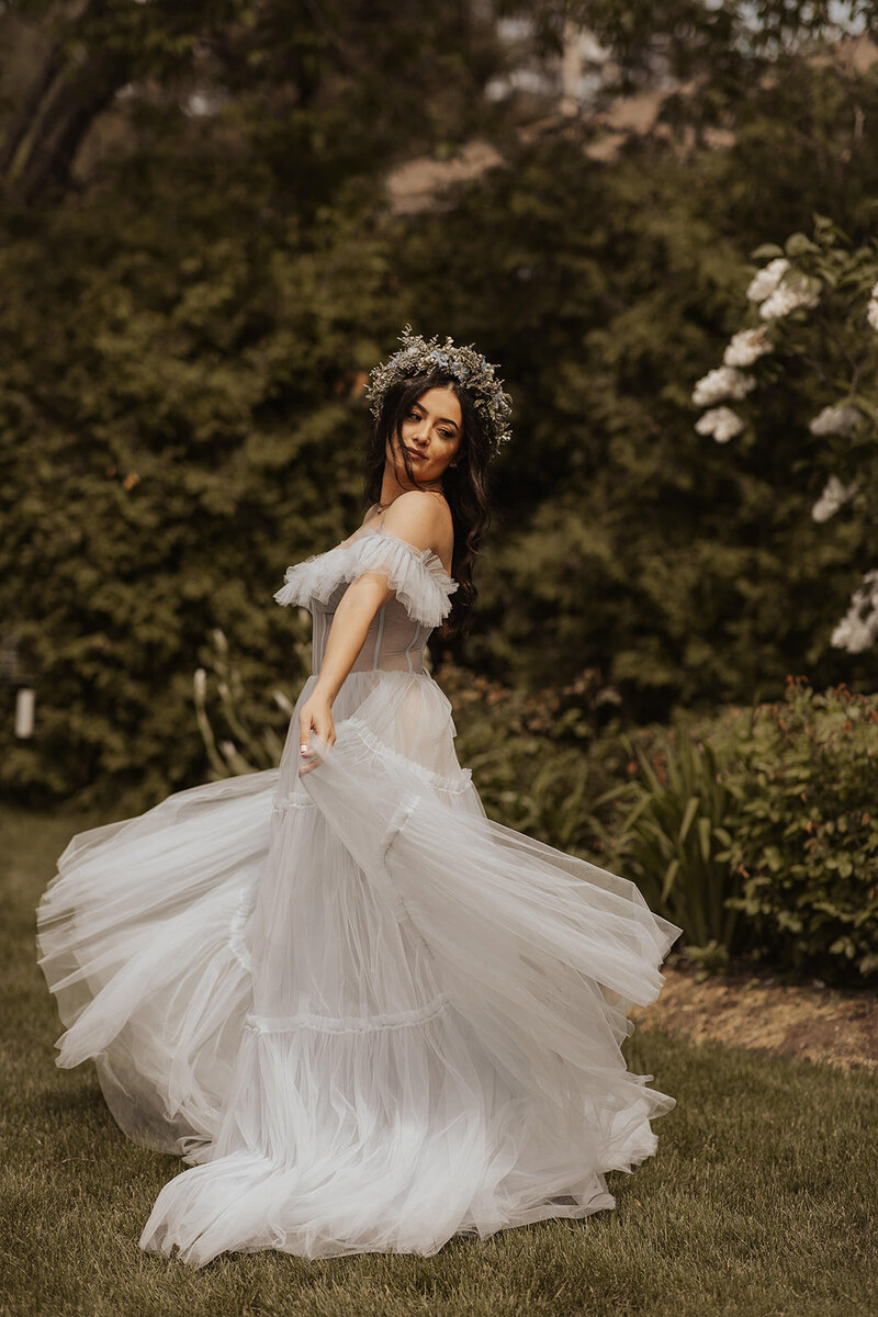 A whimsical bride in a tulle gown with a floral headpiece spins in a lush garden.