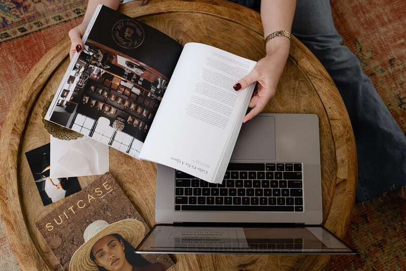 A woman's hands hold a magazine and a laptop on a wooden table, showcasing a blend of leisure and technology.