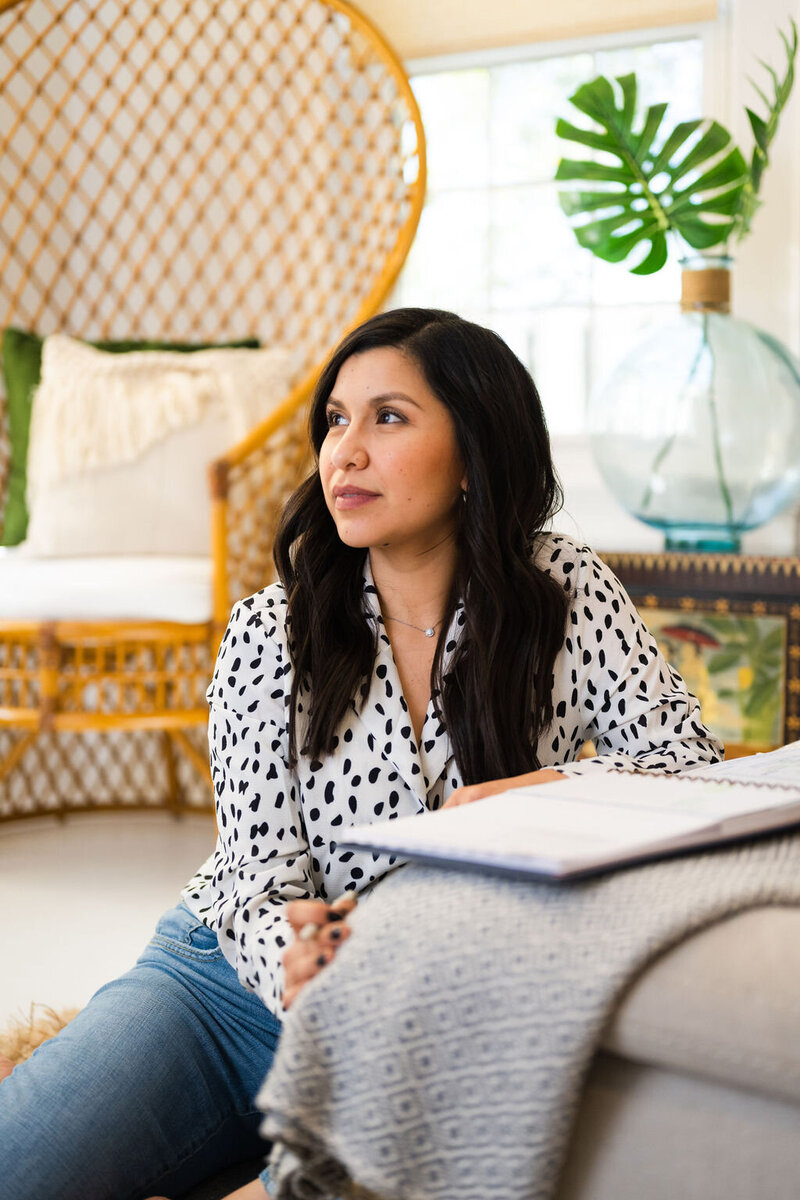 Karen wears a black and white blouse and jeans as she sits on the floor and gazes left