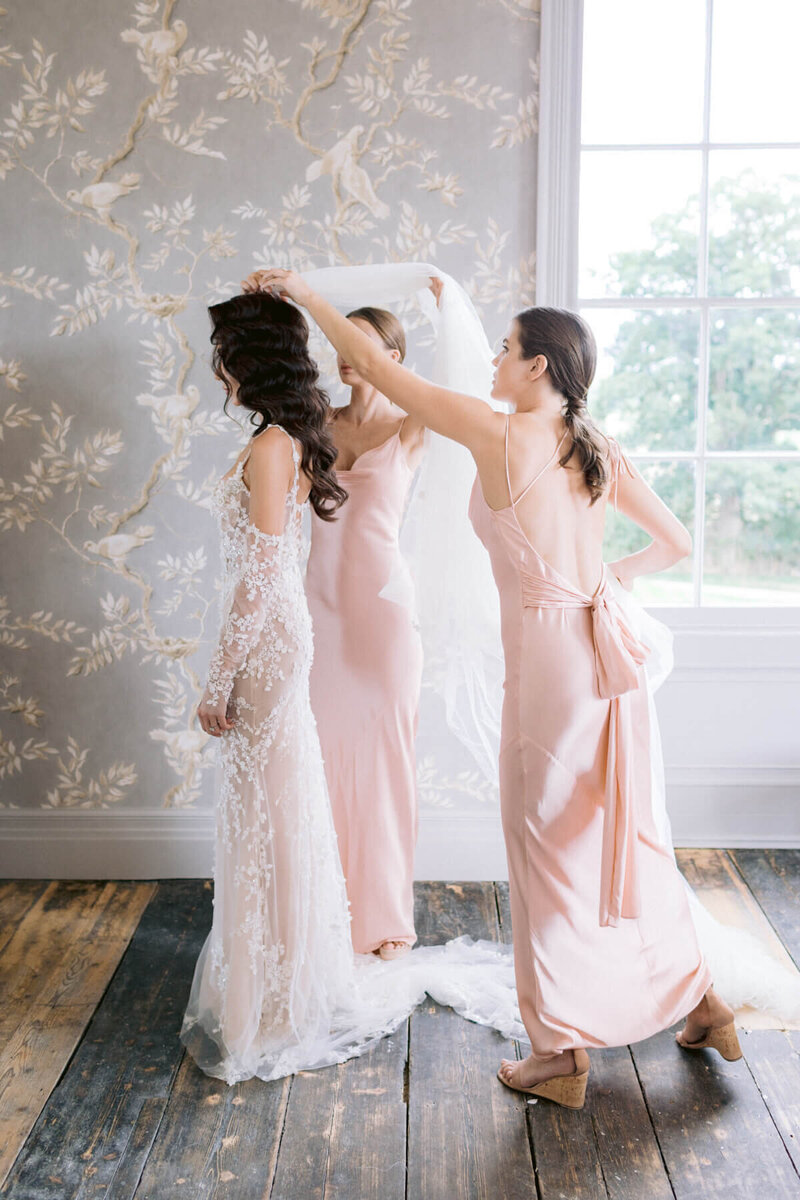 Bride getting ready with bridesmaids helping with her veil