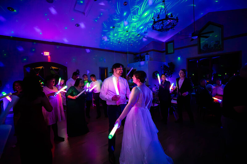 Wedding guests dancing with glow sticks under purple lights