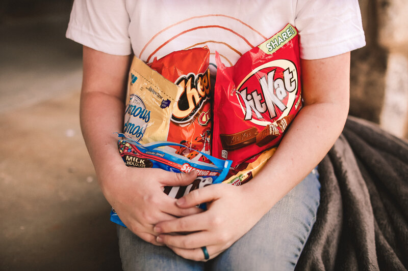 Bags of Kit-Kats, Cheetos, Cookies, and M&M's being held in the arms of a model