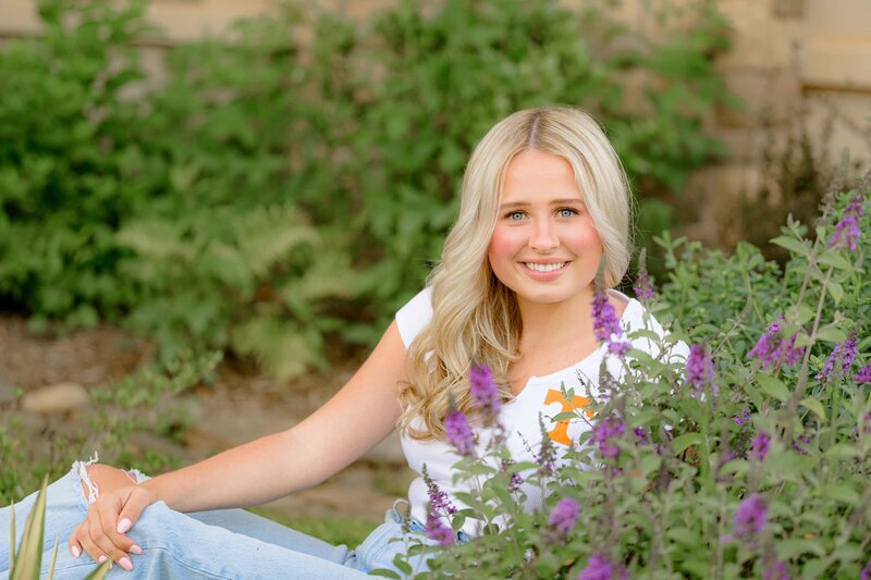 senior sits amongst purple flowers smiling wearing her future college t shirt